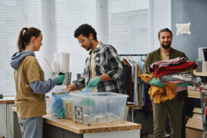 Two young volunteers sorting garbage while man carrying stack of second hand clothes while passing by behind them in After Death Cleaning Services in Bradenton