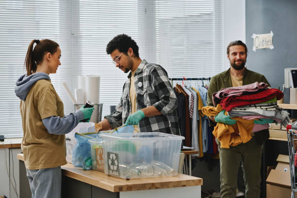 Two young volunteers sorting garbage while man carrying stack of second hand clothes while passing by behind them in After Death Cleaning Services in Bradenton