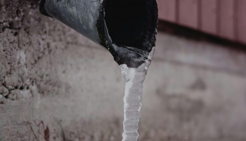 Frozen metal downspout with icicle forming at the base, showing early signs of winter pipe freezing and water damage risk.