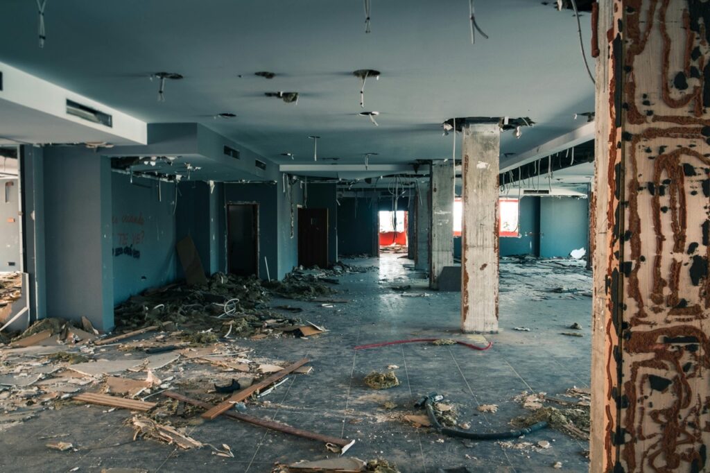 A large, dilapidated room is filled with debris, exposed wires, and damaged walls, hinting at