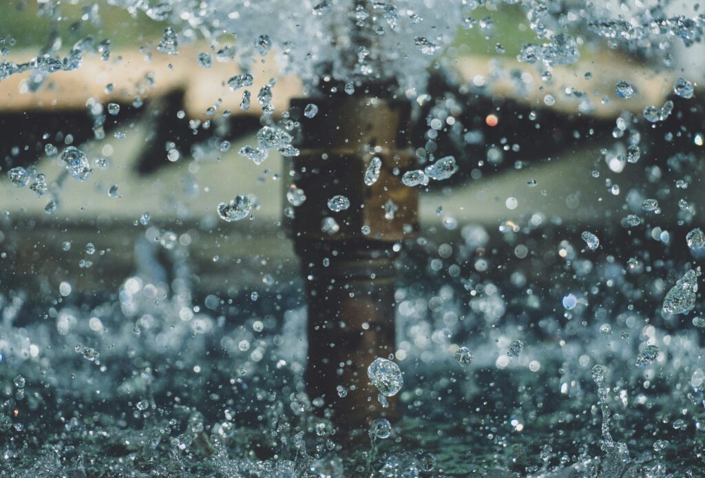 Sparkling water droplets burst from a fountain, captured mid-air against a soft, blurred background