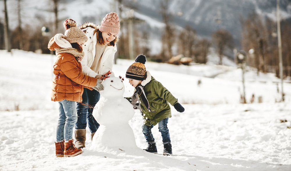 happy mother, daughter, and son building a snowman