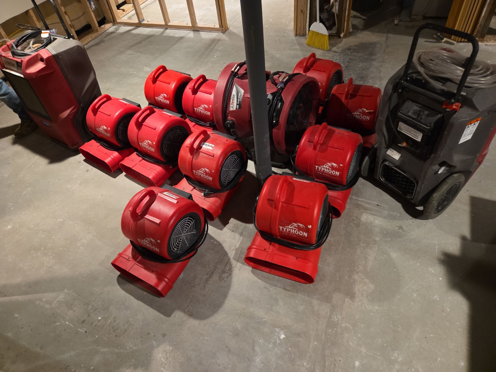 Red Typhoon air movers and large dehumidifiers are set up on a concrete floor for water damage