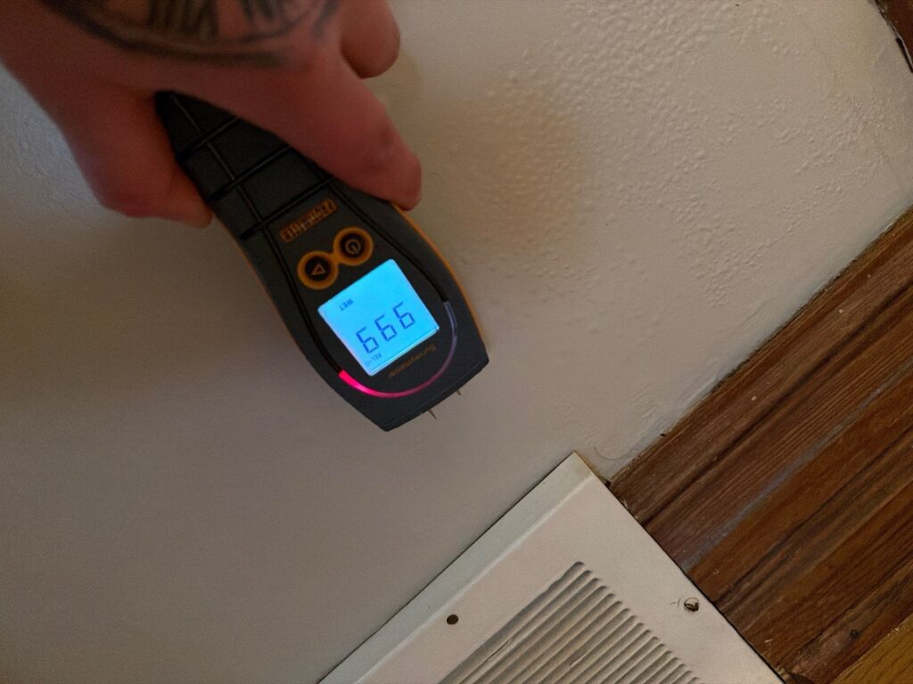 A hand holds a moisture meter displaying a 'WET' reading of 666