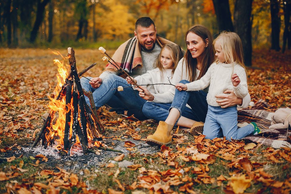 A family roasting marshmallows around a fire among fall foliage