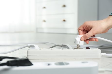 Woman inserting power plug into extension cord on floor indoors, closeup.