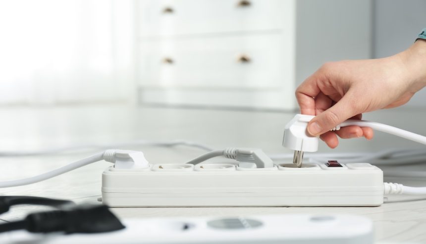 Woman inserting power plug into extension cord on floor indoors, closeup.