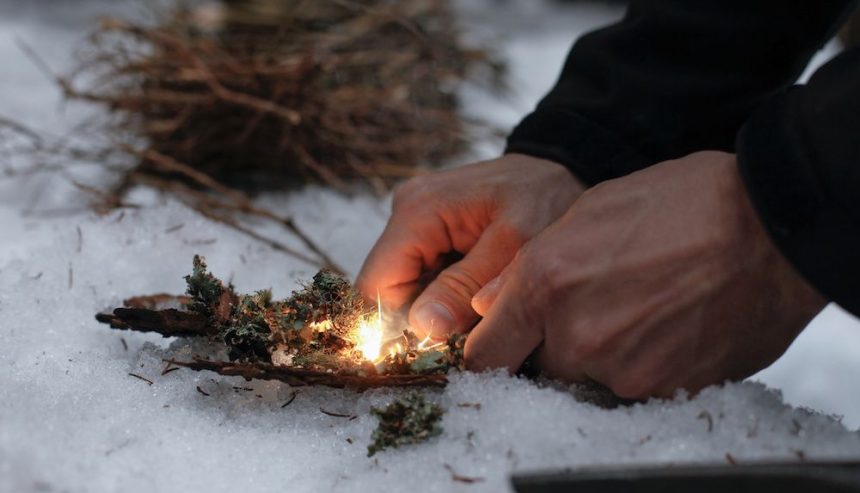Male hands starting a fire in the snow. Winter fire safety tips.