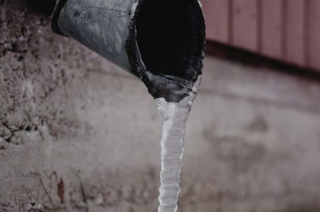 Frozen metal downspout with icicle forming at the base, showing early signs of winter pipe freezing and water damage risk.