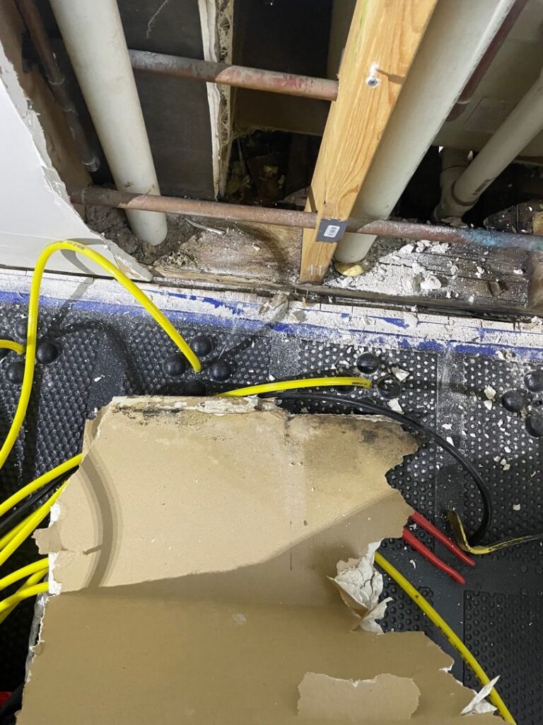 Exposed wall cavity and structural damage with mold growth, debris, and tools showing extensive water damage in a building interior.