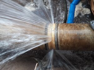Powerful streams of water erupt from a burst, rusty pipe connection.
