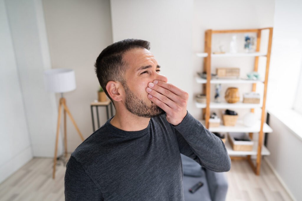 A man pinches his nose with a disgusted expression, reacting to an unpleasant smell in a