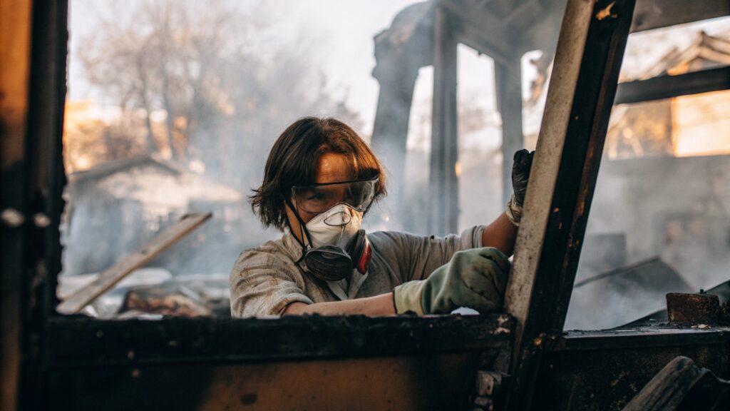 technician wearing protective goggles and a respirator mask while cleaning up debris inside a smoke-damaged structure.