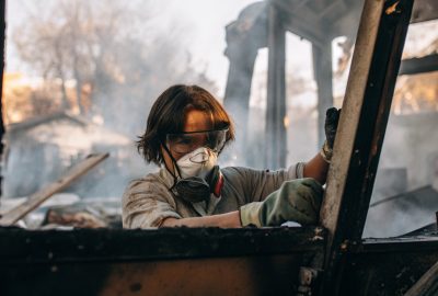 technician wearing protective goggles and a respirator mask while cleaning up debris inside a smoke-damaged structure.