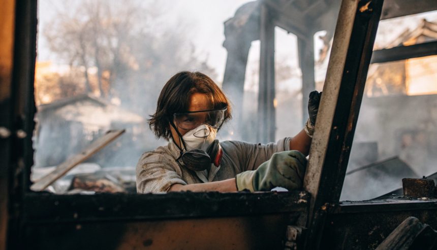 technician wearing protective goggles and a respirator mask while cleaning up debris inside a smoke-damaged structure.