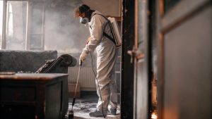 Fire damage restoration technician wearing protective gear cleaning smoke and soot inside a burned residential property