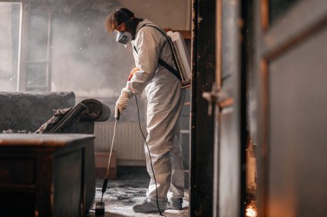 Fire damage restoration technician wearing protective gear cleaning smoke and soot inside a burned residential property