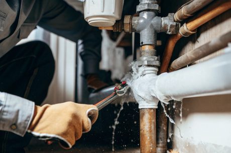 Technician repairing a frozen pipe with visible water damage, illustrating signs of water damage caused by frozen pipes in Cary, NC.