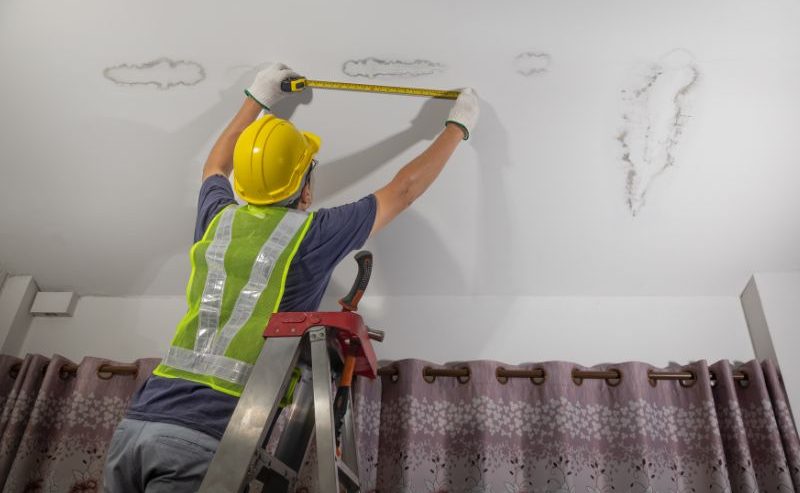 Man measuring water damage on house