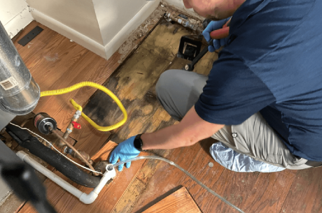 technician inspecting a flooded basement with drying fans and moisture meters visible.