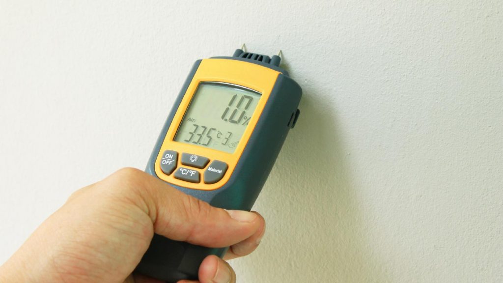 close up of a moisture meter being used to check for water damage in a drywall