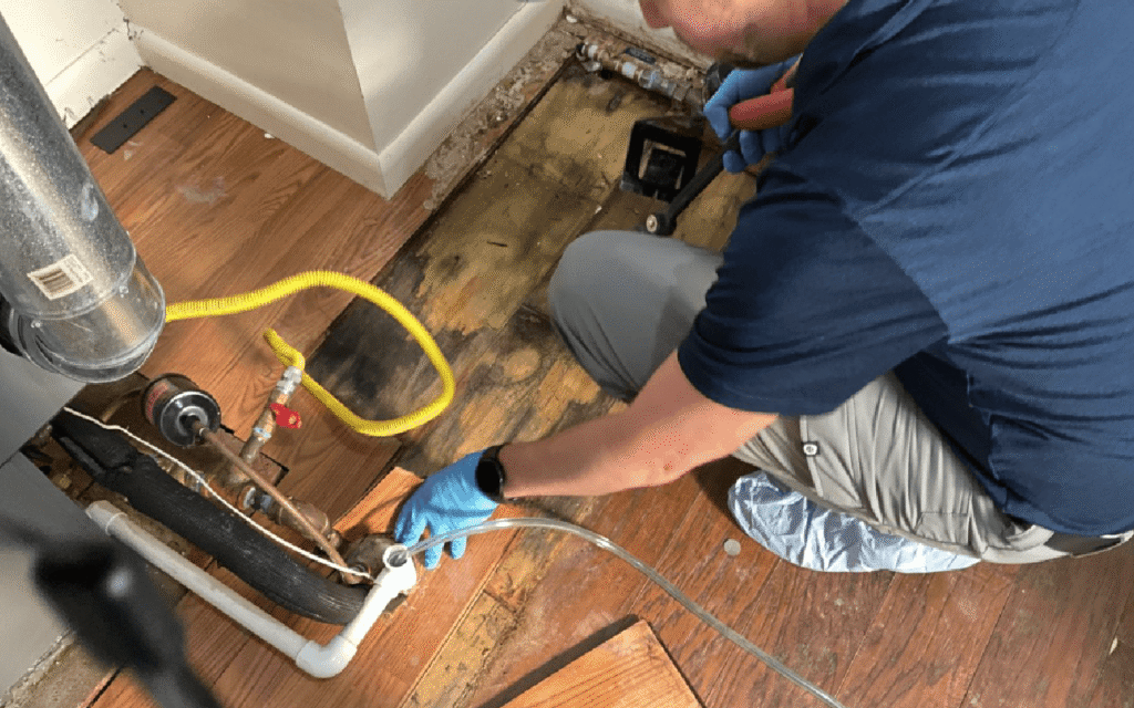 technician inspecting a flooded basement with drying fans and moisture meters visible.