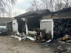 Residential fire mitigation is shown in a heavily destroyed garage structure with collapsed walls, exposed framing, and extensive fire-related debris scattered across the ground. The interior is charred and filled with burned materials, highlighting severe structural loss and smoke damage throughout the building.