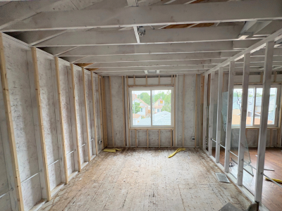 Interior view of a residential reconstruction project with exposed framing and subflooring during the early stages of code compliant reconstruction. Proper structural upgrades and layout adjustments are underway to meet local building codes and safety regulations.