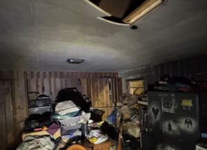 Damaged ceiling and soot-covered room showing heavy smoke damage and fire aftermath in a cluttered basement or attic.