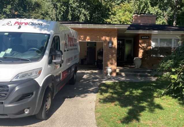 A white PuroClean service van is parked in the driveway of a brick house.