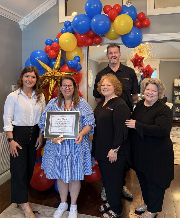 Five smiling colleagues celebrate Amy Mann's Supervisor of the Year award under a colorful balloon arch.