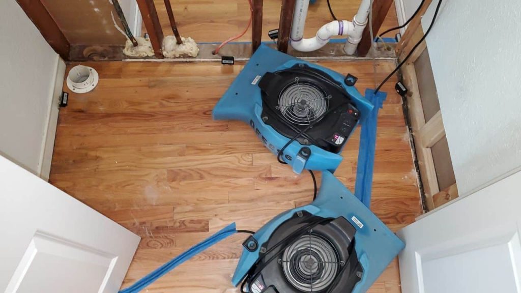 Dehumidifiers and air movers positioned throughout a flooded hallway during the drying phase