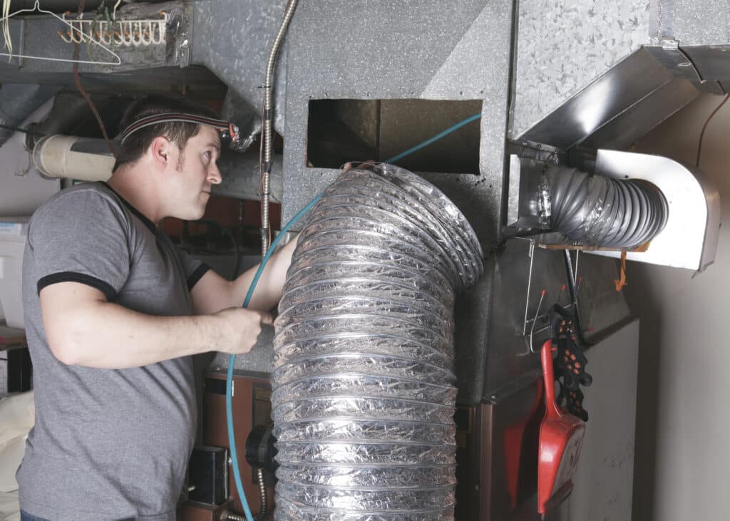 Technician inspecting ductwork inside a Covington home with HVAC panels removed