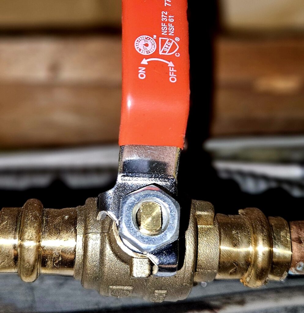 Close-up of a shut-off valve for plumbing, featuring a bright red handle and brass fittings, emphasizing water safety.