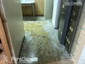 An indoor floor is covered in sewage, dirty water and debris, indicating significant damage.