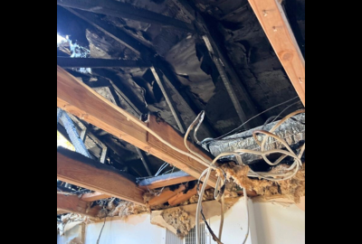 Severe ceiling and attic damage with exposed beams, wiring, and insulation after a house fire, requiring professional smoke damage restoration services.
