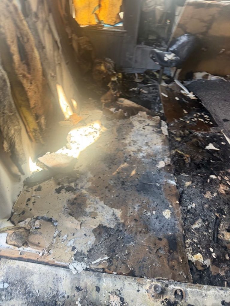 Residential fire mitigation is shown in a heavily destroyed garage structure with collapsed walls, exposed framing, and extensive fire-related debris scattered across the ground. The interior is charred and filled with burned materials, highlighting severe structural loss and smoke damage throughout the building.