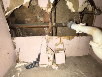 Toxic black mold infestation uncovered behind a cut-open drywall panel with visible plumbing leaks and a drywall saw on the floor.
