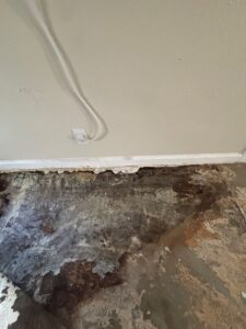 Severe water damage on concrete subfloor and deteriorating drywall near baseboards before restoration.
