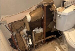 Pipe leak leads to wall drywall removal and water damage near toilet, exposing stained studs and insulation.