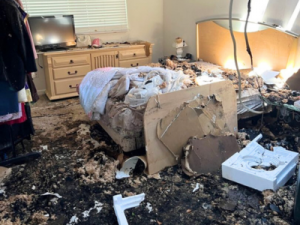Severe residential fire damage in a bedroom, including soot, debris, and destruction from smoke and heat.