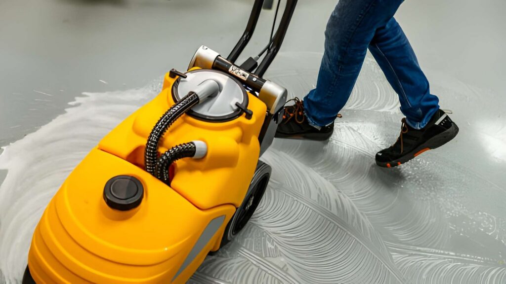 A person operates a yellow floor cleaning machine, leaving foamy suds on a light-colored
