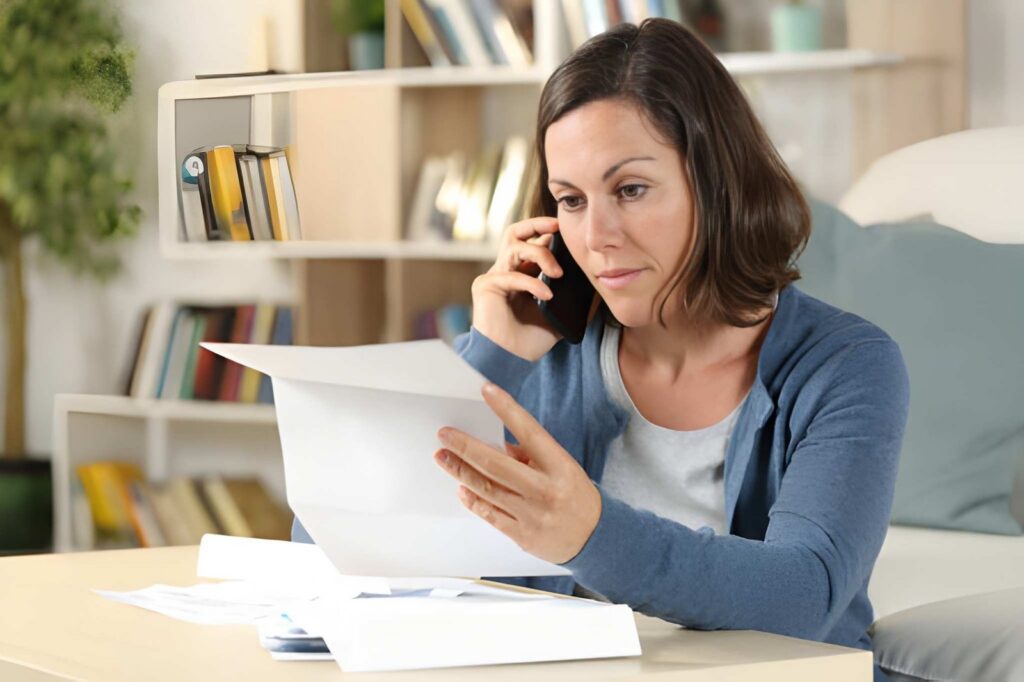 A woman with a serious expression talks on the phone and reads a document.