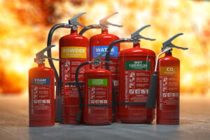 Various types of fire extinguishers in red, labeled for different uses, set against a fiery background.