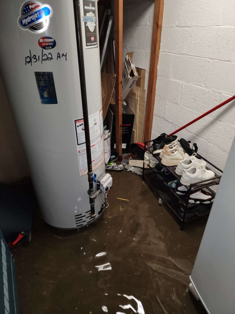 A basement floor is covered in brown floodwater around a water heater and shoe rack.