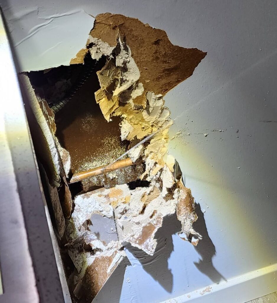A large hole in a white ceiling exposes a leaking copper pipe and significant water damage.
