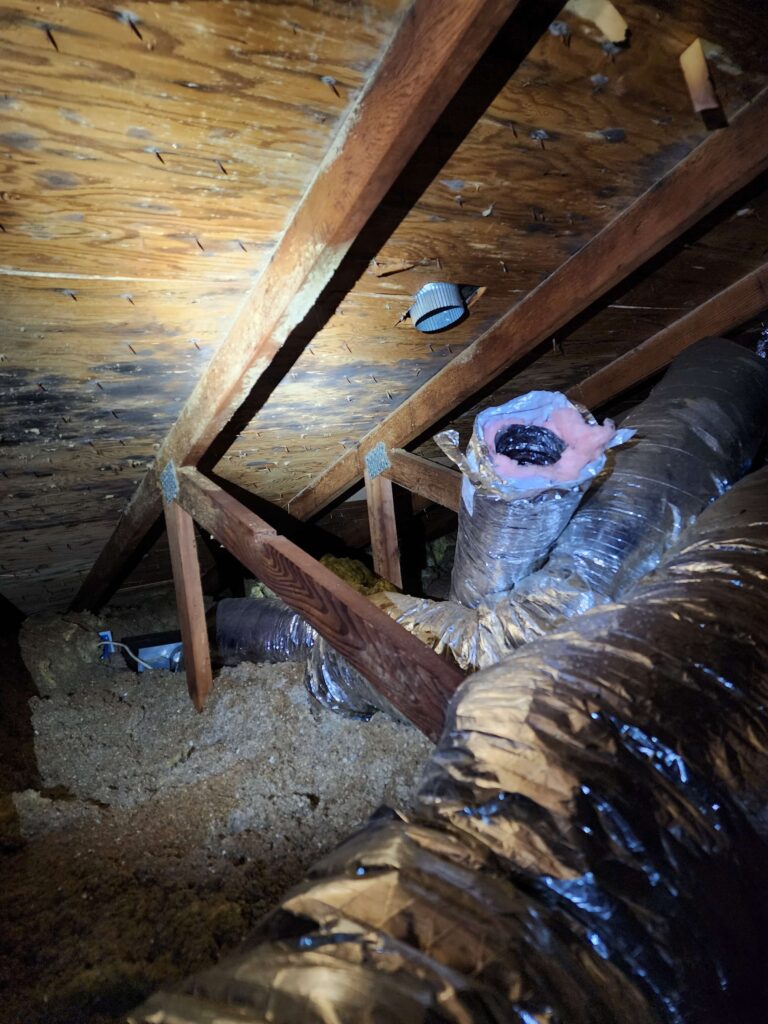 Attic interior with wooden rafters, insulation, HVAC ducts, and roof sheathing showing mold