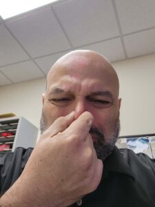 A bald man with a beard pinches his nose and squints, showing disgust at a