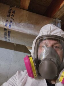 A person in a white protective suit and full-face respirator stands near a foil-