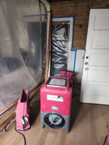 Red dehumidifier and air mover on a wooden floor in a room undergoing water damage restoration